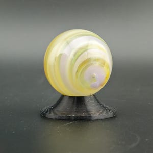 May include: A decorative glass marble with yellow, white, and purple swirls, resting on a black, spiral-shaped stand. The marble has a glossy finish and is a sphere shape.