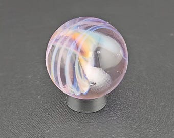 May include: A spherical glass marble featuring a translucent light purple base with swirling internal patterns of white, blue, and orange. The marble is supported by a small, circular, dark gray stand, showcasing a smooth, polished surface.
