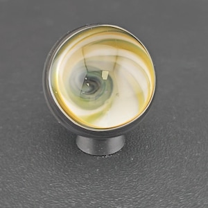 May include: A spherical cabinet knob featuring a swirling pattern of white, yellow, and dark gray glass. The knob is set into a dark metallic base, creating a smooth, rounded profile with a polished finish that reflects light across its surface.