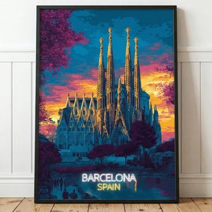 May include: A framed art print depicting the Sagrada Familia in Barcelona, Spain, at sunset. The scene features the cathedral's spires against a vibrant sky of orange, pink, and deep blue, with the text BARCELONA SPAIN printed at the bottom.