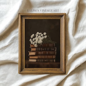 May include: A framed vintage art print depicting a stack of old books adorned with white flowers. The frame has a gold hue, and the artwork is set against a dark backdrop. The text "RALPH'S VINTAGE ART" is displayed at the top.