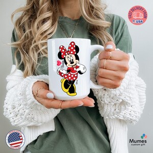 Puede incluir: Taza de cer&aacute;mica blanca con Minnie Mouse con un vestido y lazo de lunares rojos. La taza tiene un asa grande y un coraz&oacute;n con el nombre "Susan". Es un regalo personalizado.