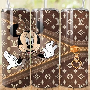 May include: A brown tumbler featuring a Minnie Mouse design with a bow and dress, set against a brown background with a zipper and a repeating pattern. The tumbler has a silver straw and lid.