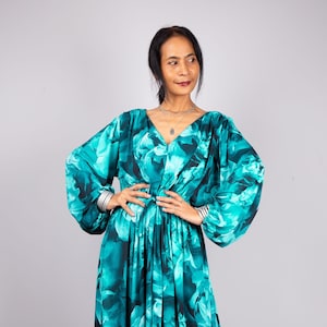 Puede incluir: Un vestido maxi largo y fluido con estampado floral en azul verdoso y negro. El vestido tiene un escote en V, mangas largas y una cintura ajustada.