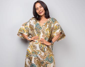 May include: A long, flowing dress with a V-neck and wide sleeves. The dress has a cream background with a repeating paisley pattern in yellow, blue, and brown. The model is wearing a watch and bracelet.