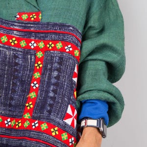 K&ouml;nnte beinhalten: Ein gr&uuml;nes, blaues und rotes gemustertes Hemd mit Kragen und langen &Auml;rmeln. Das Hemd hat ein einzigartiges Design mit geometrischen Formen und einem roten Rand. Das Hemd ist aus einem weichen, bequemen Stoff gefertigt.