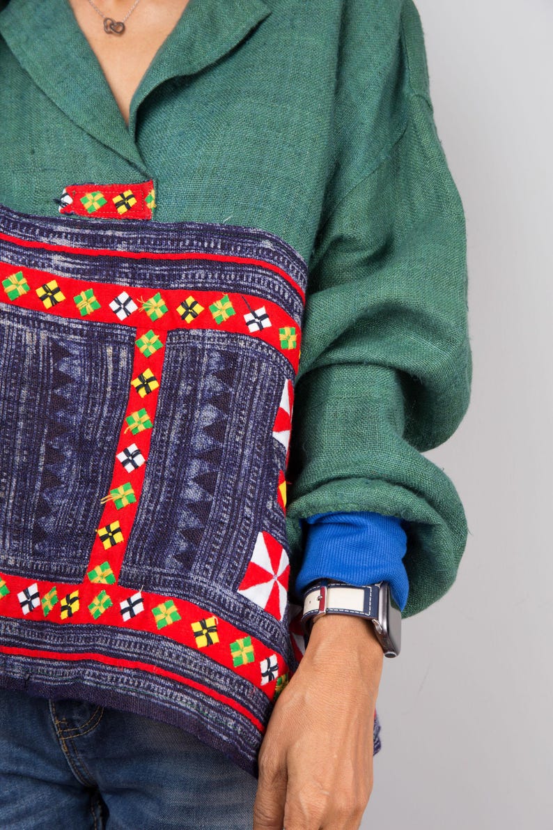 K&ouml;nnte beinhalten: Ein gr&uuml;nes, blaues und rotes gemustertes Hemd mit Kragen und langen &Auml;rmeln. Das Hemd hat ein einzigartiges Design mit geometrischen Formen und einem roten Rand. Das Hemd ist aus einem weichen, bequemen Stoff gefertigt.