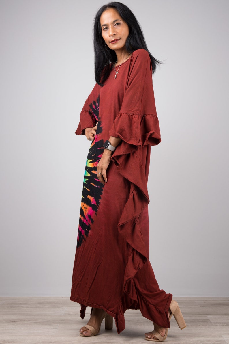 May include: A long, rust-colored maxi dress with a tie-dye design in rainbow colors. The dress has a ruffled hem and ruffled sleeves.