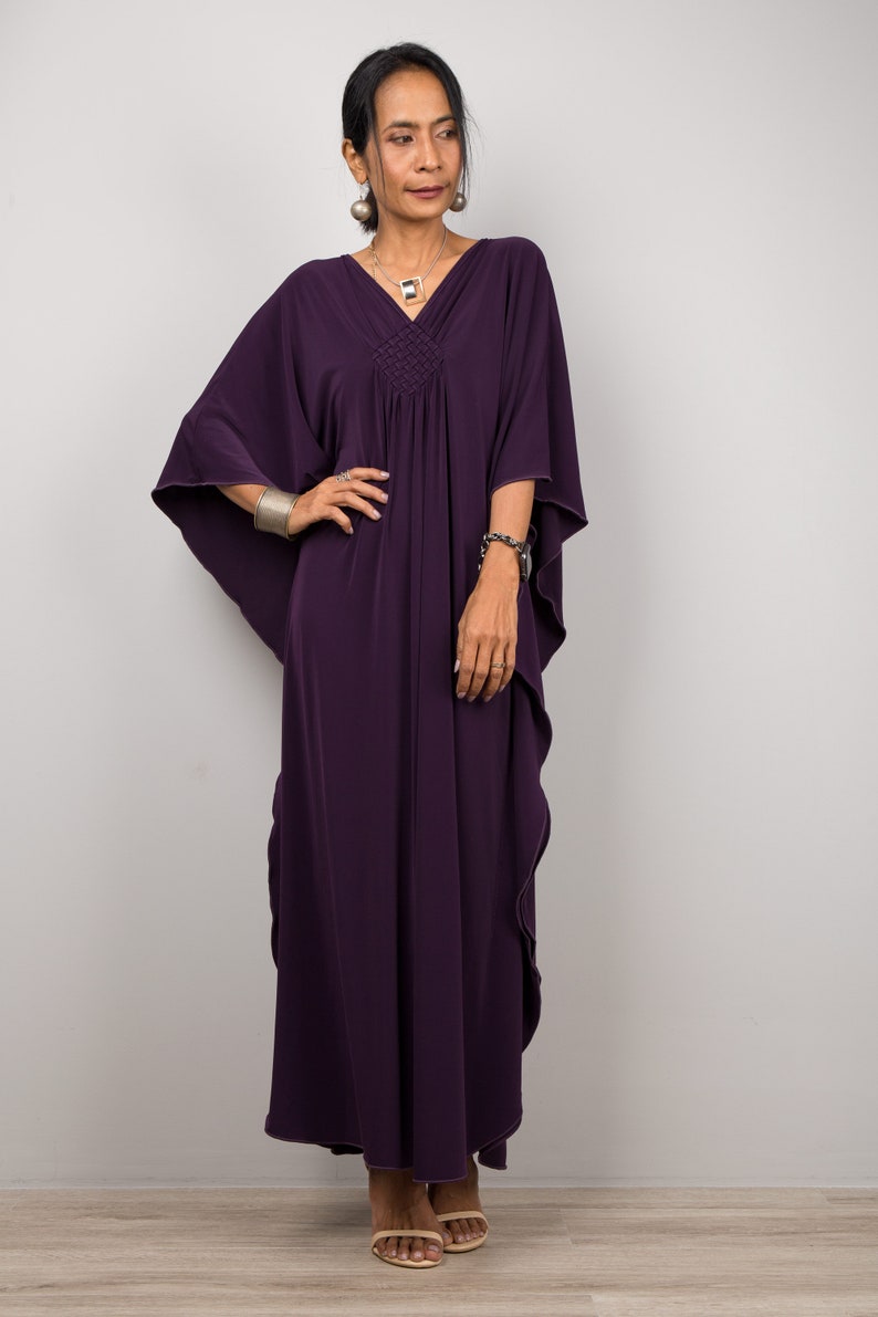 May include: A long, flowing purple kaftan dress with a V-neckline and a gathered waist. The dress has a relaxed fit and is made of a soft, comfortable fabric.