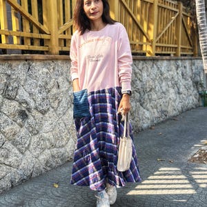 May include: A woman wearing a pink long-sleeved shirt with the text "Live like there's no tomorrow" and "Pearl City Hawaii" on the front. The shirt is paired with a blue and white plaid skirt and white sneakers. She is carrying a white handbag.