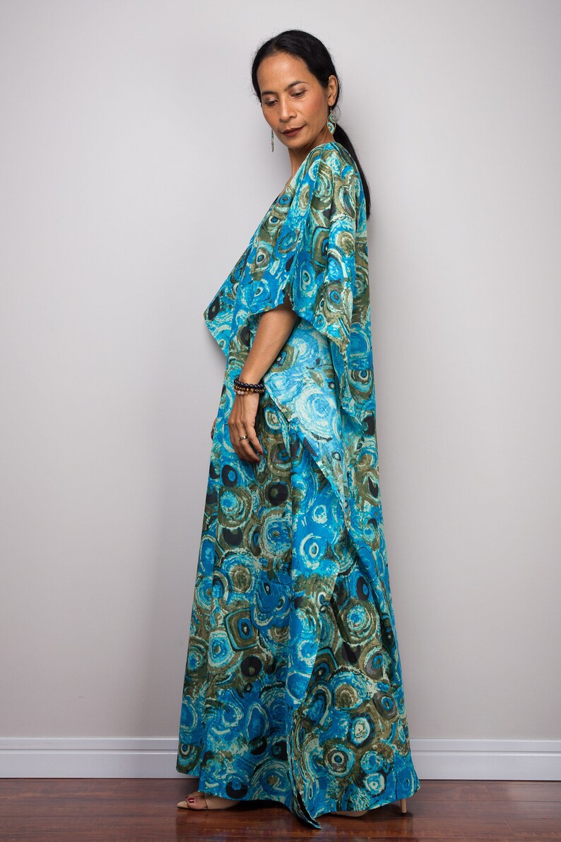 May include: A long, flowing blue and green patterned maxi dress with a draped neckline and short sleeves. The dress has a unique, abstract print that resembles swirling patterns.
