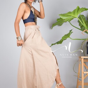 May include: A woman wearing a navy blue crop top and a beige maxi skirt with a side slit. She is wearing silver bracelets and a necklace. The skirt is made of a lightweight fabric and has a flowing silhouette. The woman is standing in front of a grey wall with a potted plant in the background.