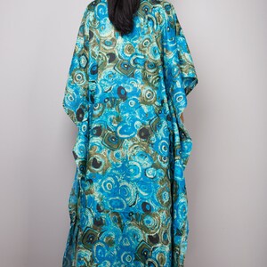 May include: A long, flowing blue and green kaftan with a swirling, abstract pattern. The kaftan has a V-neck and short sleeves.