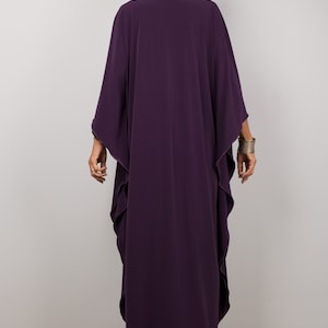 May include: A long, flowing purple kaftan with a wide, open neckline. The kaftan has a relaxed fit and is made of a soft, drapey fabric.