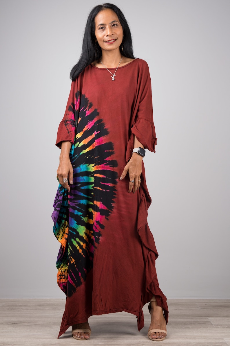 May include: A long, rust-colored, tie-dye dress with a rainbow and black swirl design. The dress has a ruffled hem and three-quarter sleeves.