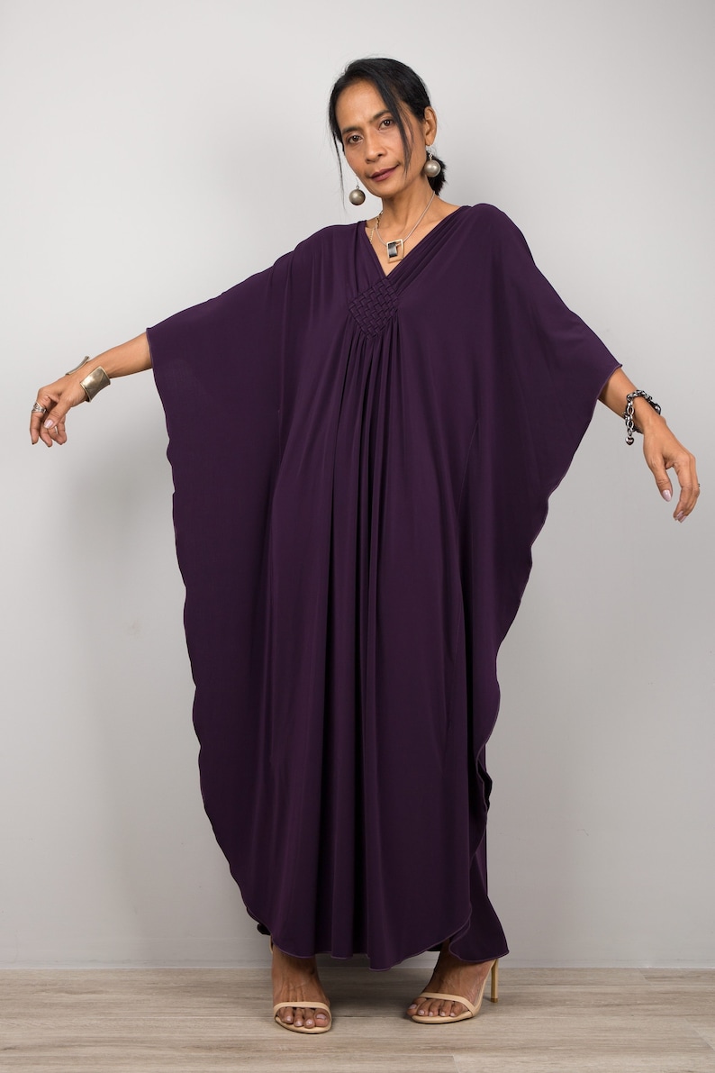 May include: A woman wearing a long, flowing purple kaftan with a gathered neckline. She is wearing silver earrings and a silver necklace.