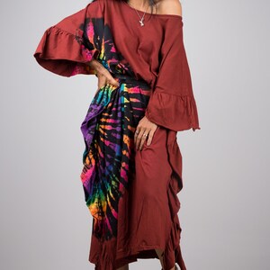 May include: A woman wearing a maroon maxi dress with a colorful tie-dye print skirt. The dress has a ruffled hem and sleeves. She is wearing sandals and a silver necklace.