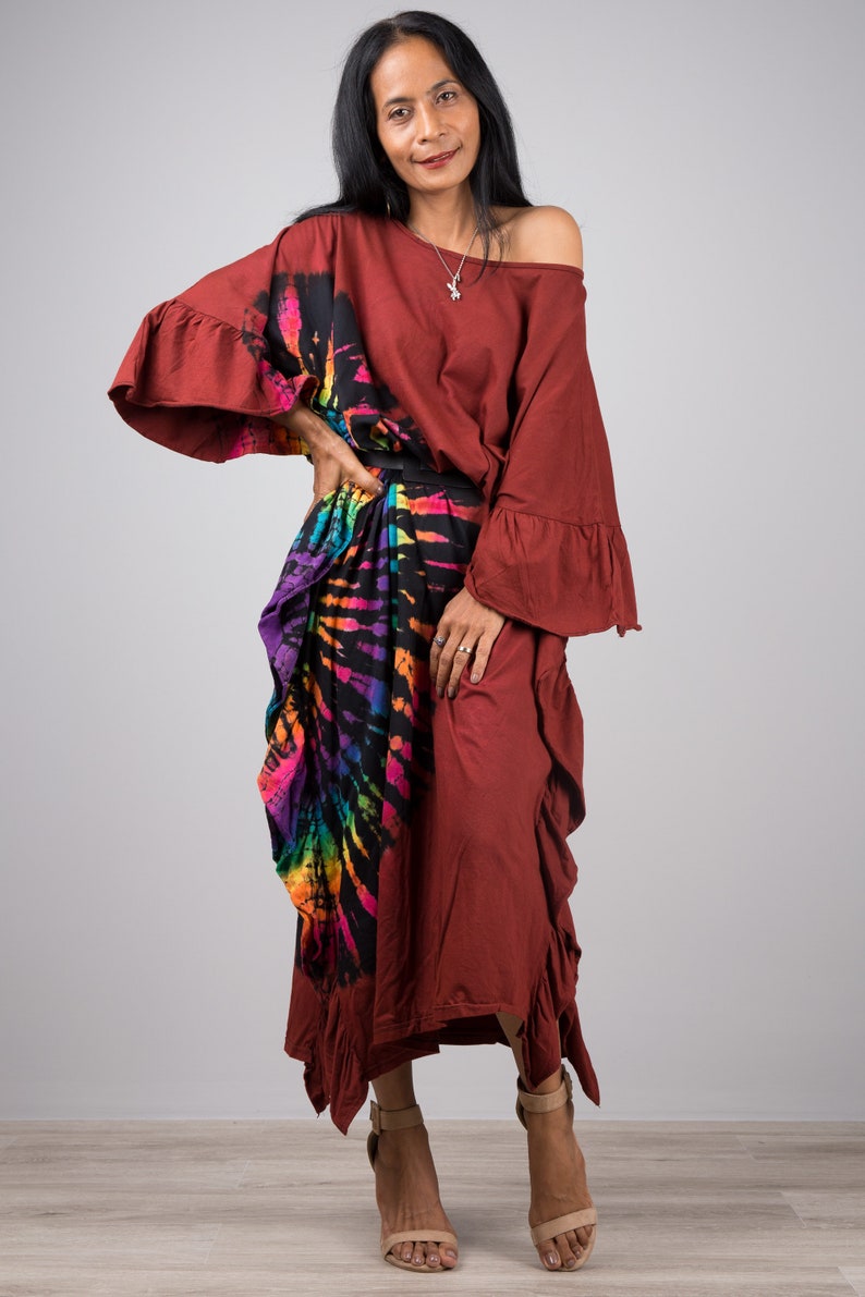 May include: A woman wearing a maroon maxi dress with a colorful tie-dye print skirt. The dress has a ruffled hem and sleeves. She is wearing sandals and a silver necklace.