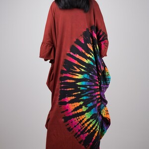 May include: A long, rust-colored, tie-dye dress with a rainbow and black circular design on the back. The dress has a loose fit and a ruffled hem.