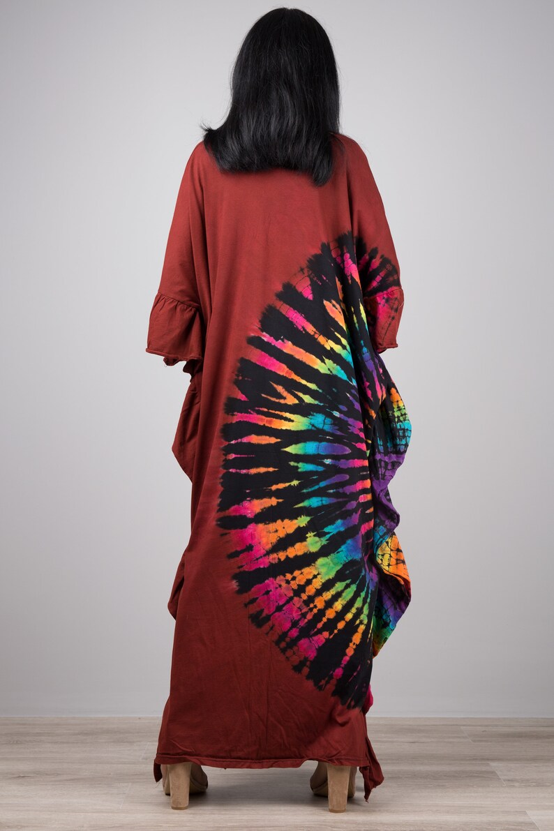 May include: A long, rust-colored, tie-dye dress with a rainbow and black circular design on the back. The dress has a loose fit and a ruffled hem.