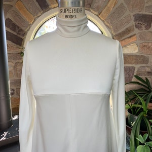 Peut inclure: Une robe cr&egrave;me &agrave; manches longues avec un col roul&eacute;. La robe est pr&eacute;sent&eacute;e sur un mannequin. La robe a une couture sur la section m&eacute;diane. Le mannequin est &eacute;tiquet&eacute; "SUPERIOR MODEL".