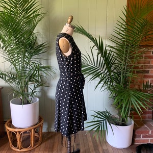 May include: A black and white polka dot dress with a fitted bodice and a flowing skirt. The dress has a tie at the waist and is sleeveless.