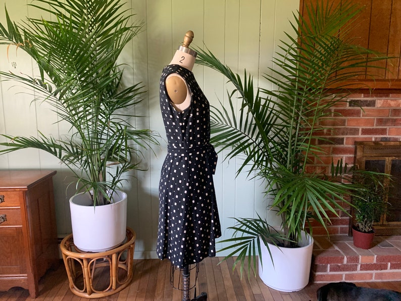 May include: A black and white polka dot dress with a fitted bodice and a flowing skirt. The dress has a tie at the waist and is sleeveless.