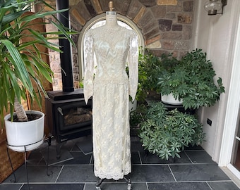 May include: Ivory-colored wedding dress with long sleeves and intricate lace detailing. The dress is displayed on a mannequin, showcasing its fitted bodice and flowing skirt. The lace design is visible on the sleeves, bodice, and skirt, creating a delicate and elegant look.