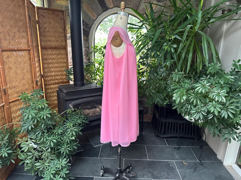 Puede incluir: Un camis&oacute;n rosa vintage exhibido en un maniqu&iacute;. El camis&oacute;n presenta un dise&ntilde;o fluido hasta el suelo con un delicado ribete de encaje alrededor del escote. El color rosa suave y la tela ligera sugieren una opci&oacute;n de ropa de dormir c&oacute;moda y elegante.