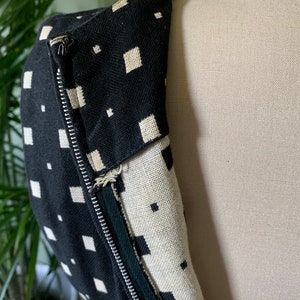 May include: Black and white geometric patterned fabric with a zipper closure. The fabric is a close-up of a garment.
