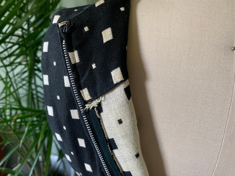 May include: Black and white geometric patterned fabric with a zipper closure. The fabric is a close-up of a garment.