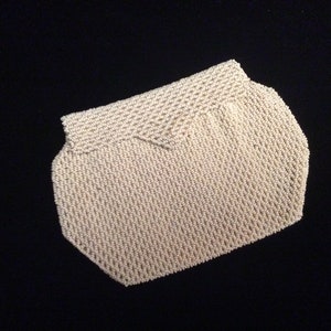 Op de afbeelding: Off-white kralen clutch met een geometrische vorm. De tas heeft een klepsluiting en is gemaakt van kleine, dicht geweven kralen. De achtergrond is effen zwart.