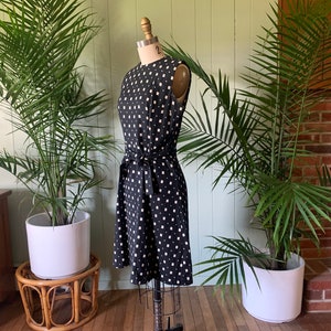 May include: A black and white sleeveless dress with a geometric pattern. The dress has a tie belt at the waist and is on a dress form.