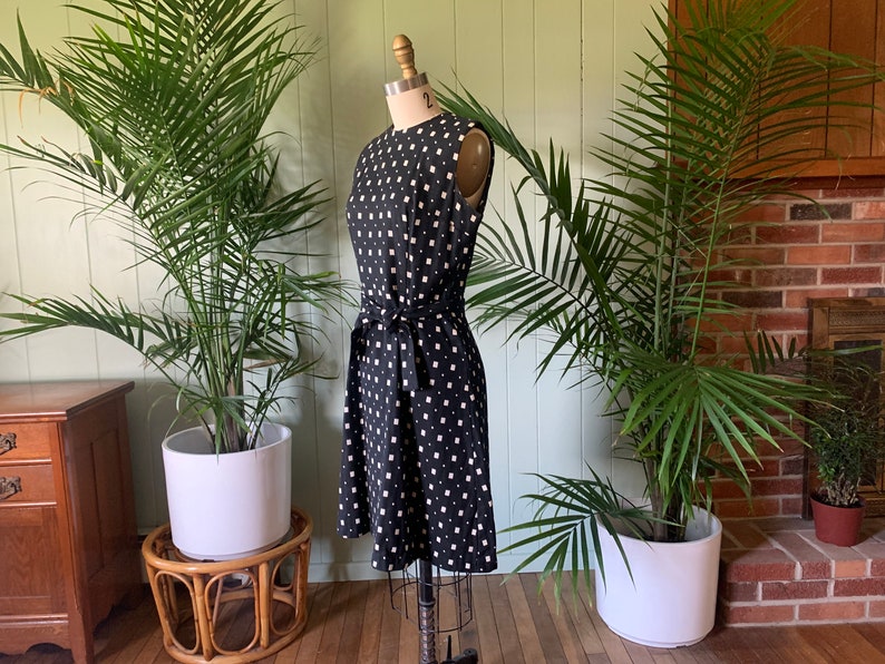 May include: A black and white sleeveless dress with a geometric pattern. The dress has a tie belt at the waist and is on a dress form.