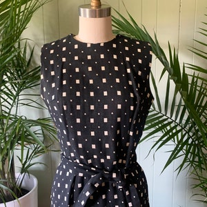 May include: A sleeveless black and white dress with a geometric pattern. The dress has a fitted bodice and a skirt with a tie belt.