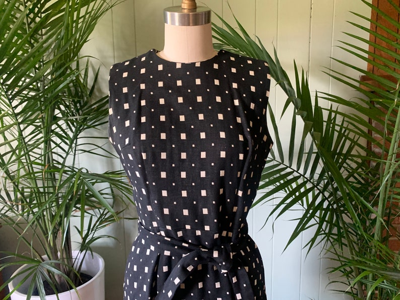 May include: A sleeveless black and white dress with a geometric pattern. The dress has a fitted bodice and a skirt with a tie belt.