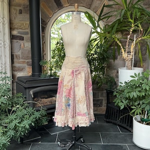 Op de afbeelding: Een crèmekleurige midirok met een ontwerp van meerdere panelen met diverse bloemen- en botanische patronen in tinten roze, blauw en beige. De rok heeft een geplooide, elastische tailleband en een uitlopend silhouet met een rucheszoom.