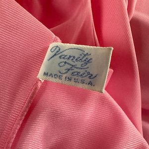 Puede incluir: Primer plano de una tela rosa con una etiqueta que dice "Vanity Fair MADE IN U.S.A." La tela tiene una textura suave y sedosa, posiblemente una prenda. La etiqueta es rectangular con texto azul.