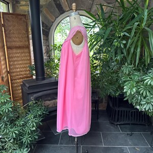 Puede incluir: Un camis&oacute;n rosa vintage en un maniqu&iacute;. El camis&oacute;n es de color rosa vibrante con detalles de encaje alrededor del escote y el dobladillo. La tela parece ligera y fluida. El maniqu&iacute; se exhibe en una habitaci&oacute;n con plantas y una chimenea.