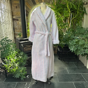May include: A full-length, light pink robe with vertical stripes of blue and pink. The robe has a shawl collar, rolled cuffs, and a matching belt. The robe is displayed on a mannequin, suggesting it's for sale.