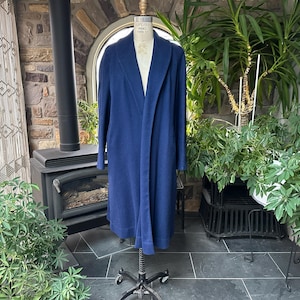 Könnte beinhalten: Ein langer, einfarbiger marineblauer Mantel mit Schalkragen und langen Ärmeln, präsentiert auf einer Schneiderpuppe. Der Mantel hat ein gerades, offenes Design mit glatter Textur und einem Saum, der unter die Knie reicht, was eine einfache, strukturierte Silhouette ergibt.