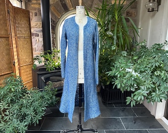 May include: A long, open-front cardigan in shades of blue, displayed on a mannequin. The knitwear features a textured pattern and a flowing, floor-length design. The cardigan is approximately 152 cm long.