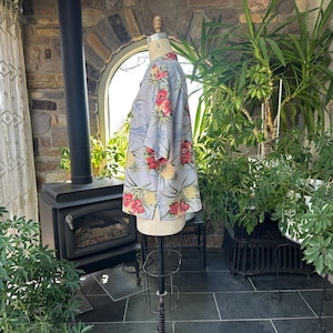 Może przedstawiać: Jasnoniebieska koszula z tropikalnym wzorem kwiatowym z czerwonych kwiat&oacute;w i ż&oacute;łtych ananas&oacute;w. Koszula jest prezentowana na manekinie. Tło obejmuje rośliny, kominek i okno.