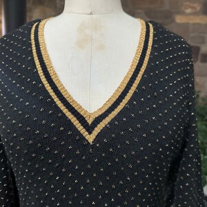 Pu&ograve; includere: Maglione nero a maglia con scollo a V e dettagli dorati. Il maglione ha un bordo dorato intorno allo scollo e piccoli punti dorati su tutto il tessuto. Il maglione &egrave; esposto su un manichino.