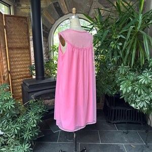 Puede incluir: Un camis&oacute;n rosa vintage en un maniqu&iacute;. El camis&oacute;n sin mangas tiene un canes&uacute; transparente con adornos decorativos y una falda fluida hasta la rodilla. La tela parece ligera y el estilo es cl&aacute;sico.