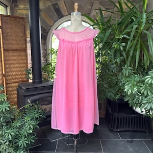 Puede incluir: Un camis&oacute;n rosa vintage en un maniqu&iacute;. El camis&oacute;n tiene un canes&uacute; transparente y mangas cortas con un ribete con volantes. El vestido largo y fluido est&aacute; hecho de una tela ligera. El maniqu&iacute; est&aacute; sobre un soporte de metal, con plantas y una chimenea en el fondo.
