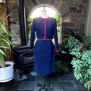 May include: A navy blue corduroy skirt suit with a red trim. The jacket has a round neckline and button closure. The skirt is knee-length.