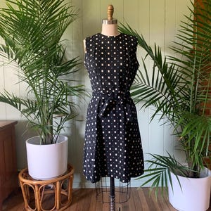 May include: A black and white sleeveless dress with a geometric pattern. The dress has a fitted bodice and a slightly flared skirt. It features a belt at the waist.