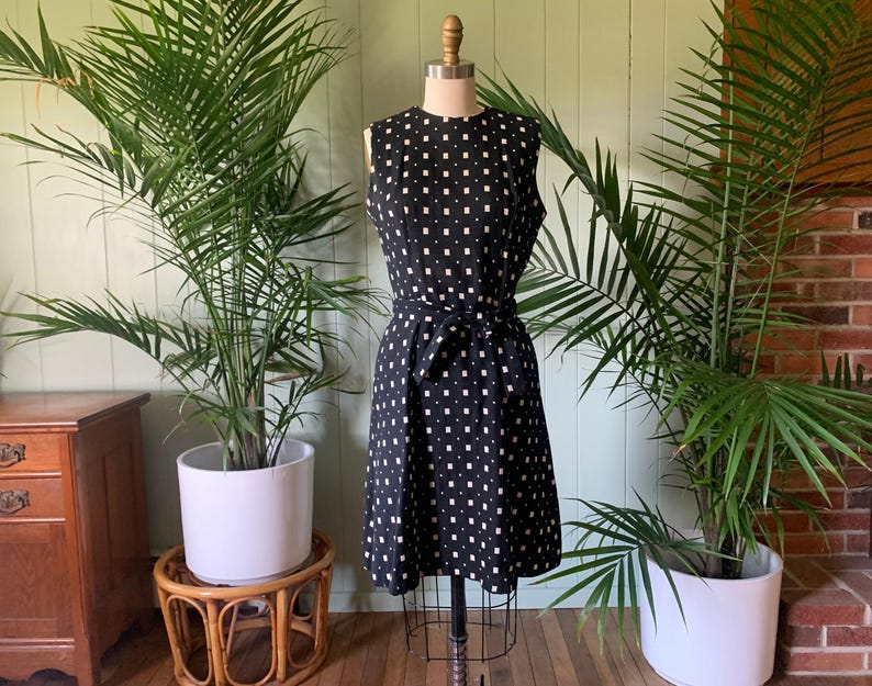May include: A black and white sleeveless dress with a geometric pattern. The dress has a fitted bodice and a slightly flared skirt. It features a belt at the waist.