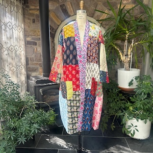 May include: A long-sleeved robe featuring a patchwork design composed of various floral and geometric fabric patterns in shades of red, blue, yellow, white, and pink. The garment has an open front, a straight hem, and a collarless neckline.